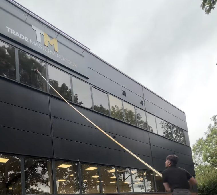An exterior wall being soft washed with a pole system